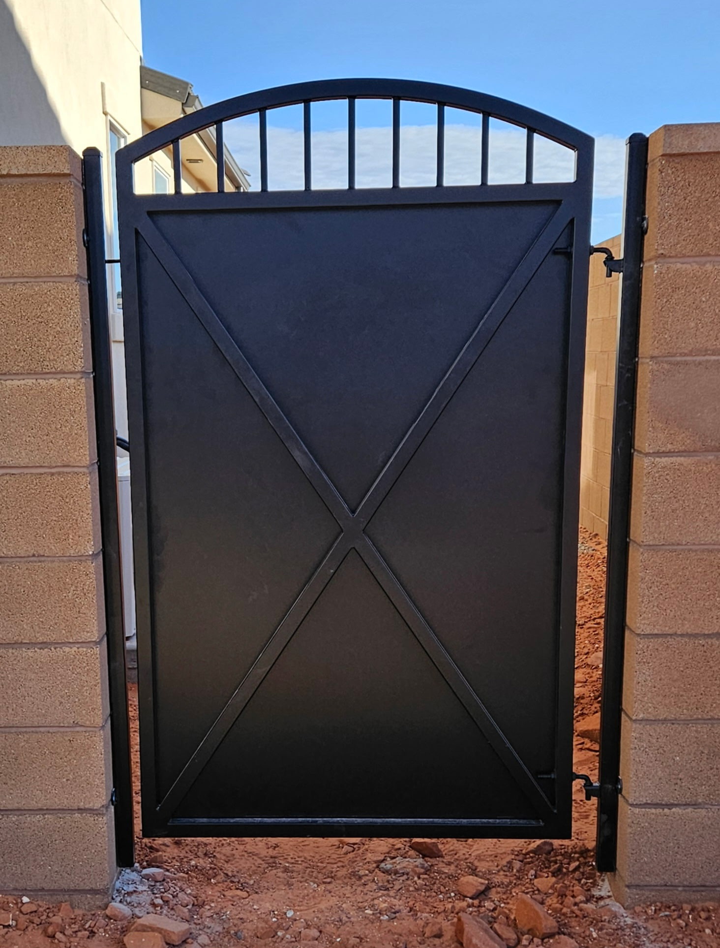 Custom black steel privacy gate with arched top, vertical pickets, and X-brace design between block wall pillars in St. George, Utah
