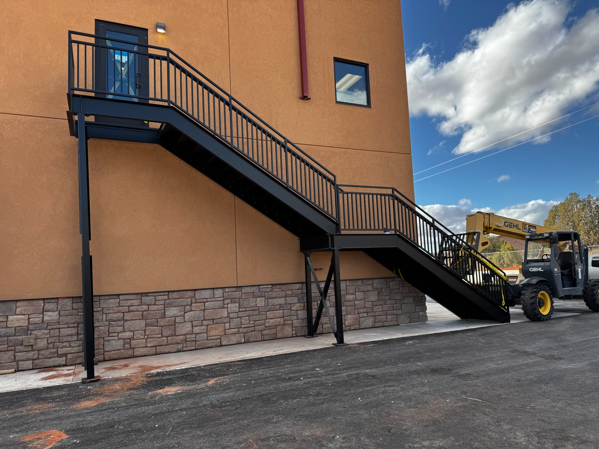 Black structural steel exterior staircase with two flights, a mid-level landing, and picket guardrails leading to a second-story door on a commercial building in Southern Utah