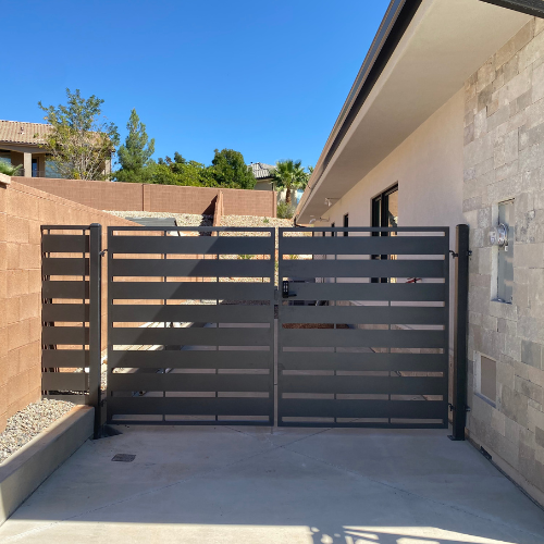 Modern double swing steel gate with wide horizontal slats and a matching side panel next to a block wall and stone veneer home in St. George, Utah