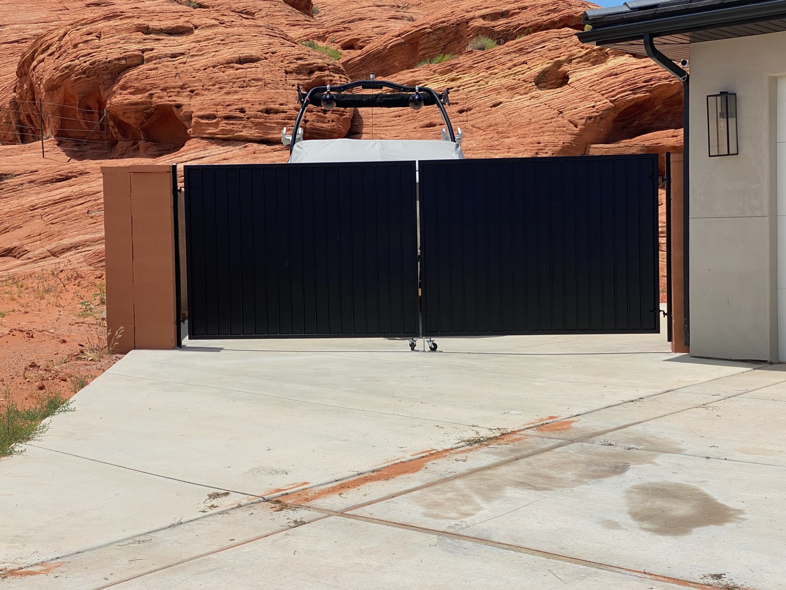 Black steel double swing RV and boat gate with vertical ribbed privacy panels installed across a concrete driveway in front of red sandstone rock formations in St. George, Utah