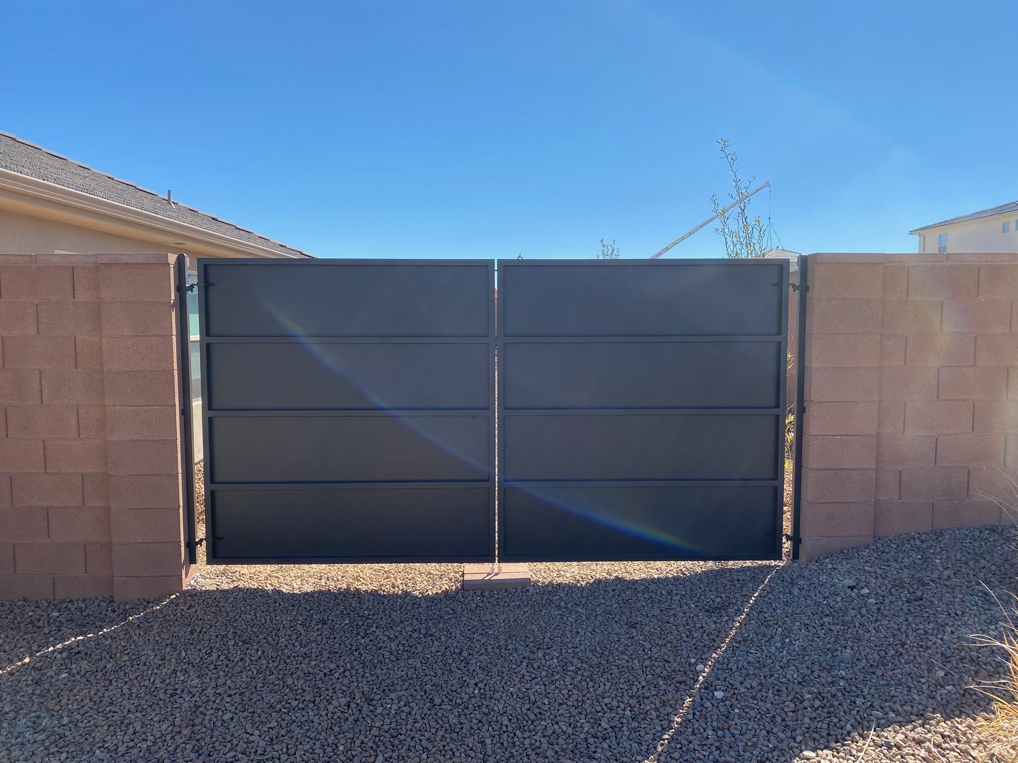 Solid black steel double swing RV gate with horizontal panel sections installed between block wall pillars over a gravel driveway in St. George, Utah