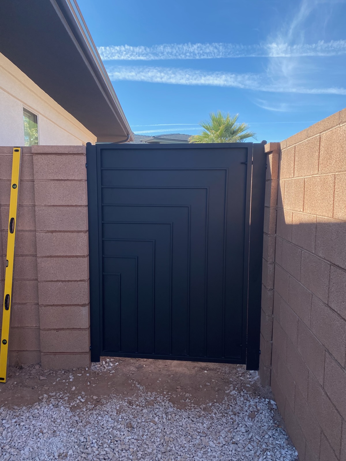 Solid black steel privacy gate with a raised geometric pattern of nested right-angle lines, installed between tan block wall pillars in St. George, Utah