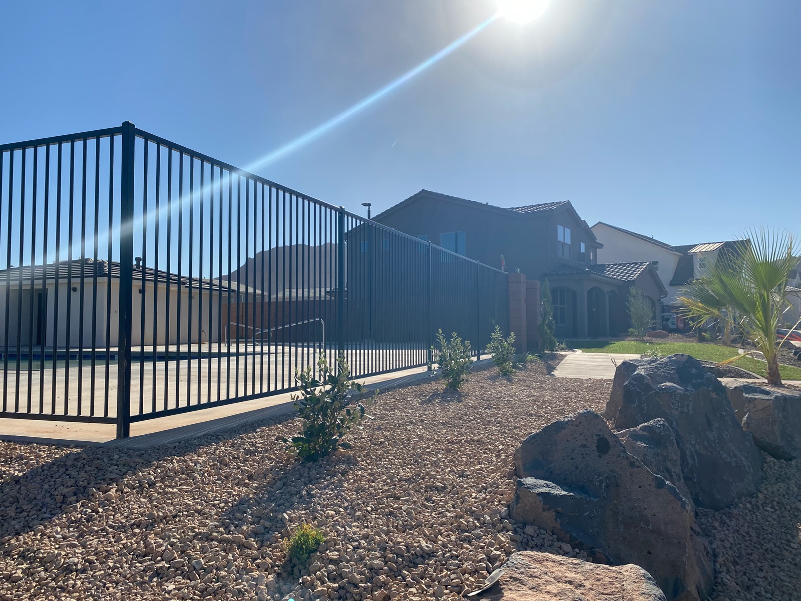 Tall black steel picket pool fence surrounding a swimming pool deck, bordered by desert landscaping with boulders and gravel in St. George, Utah