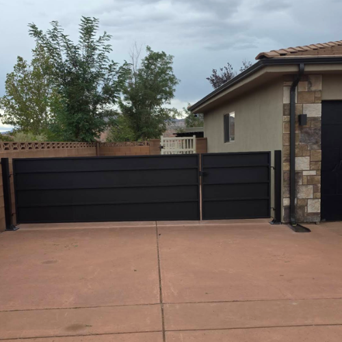 Black steel unequal double swing gate with horizontal privacy panels between a block wall with decorative breeze block and a stone veneer garage in Southern Utah